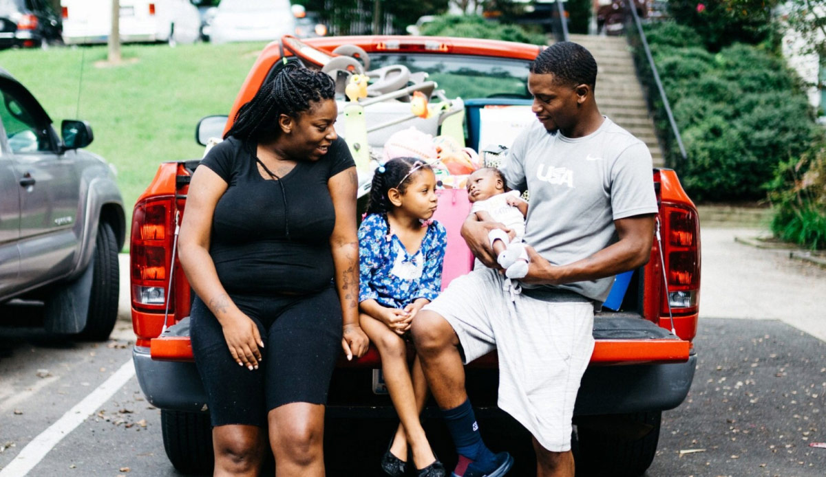 family sitting on tailgate of pickup truck with belongings