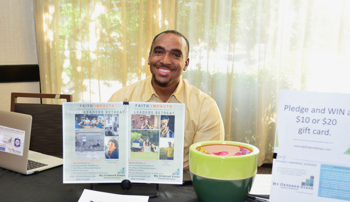 man sitting at table displaying flyer for Faith Impacts Leaders Retreat